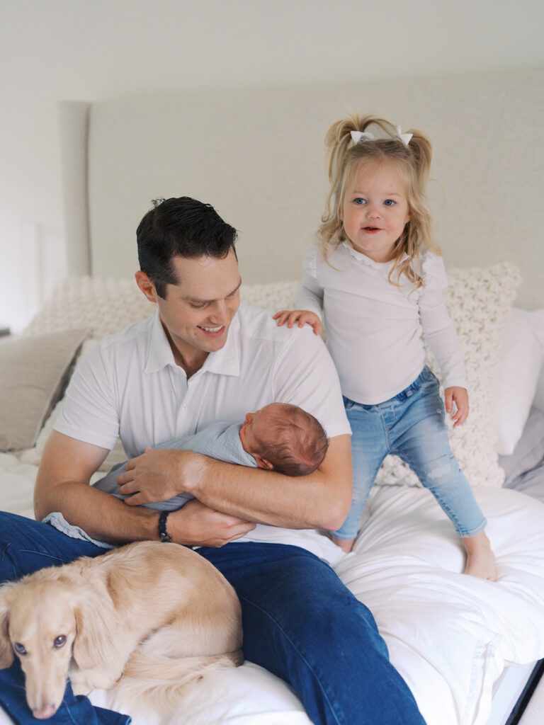 Dad with toddler daughter and newborn son on the bed during a newborn session by newborn photographer Tanya Zagumenov