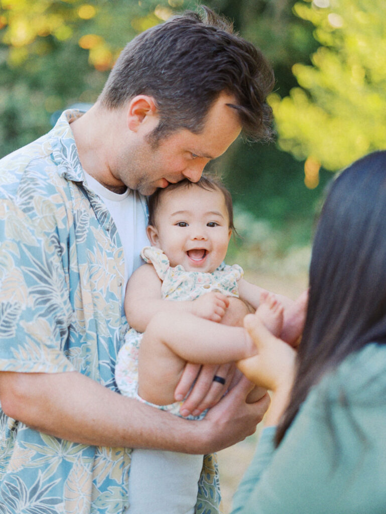 Mom tickles baby's toes while dad kisses baby during a backyard family session in Seattle