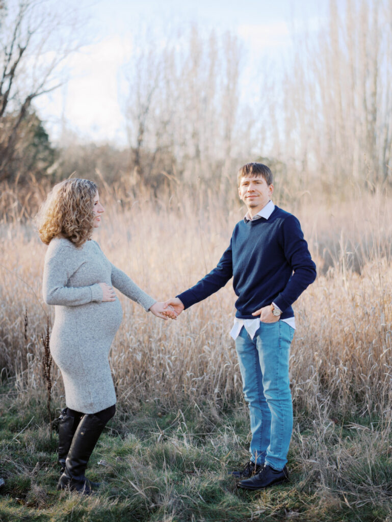A pregnant mom and her husband standing apart and holding hands in a Seattle park