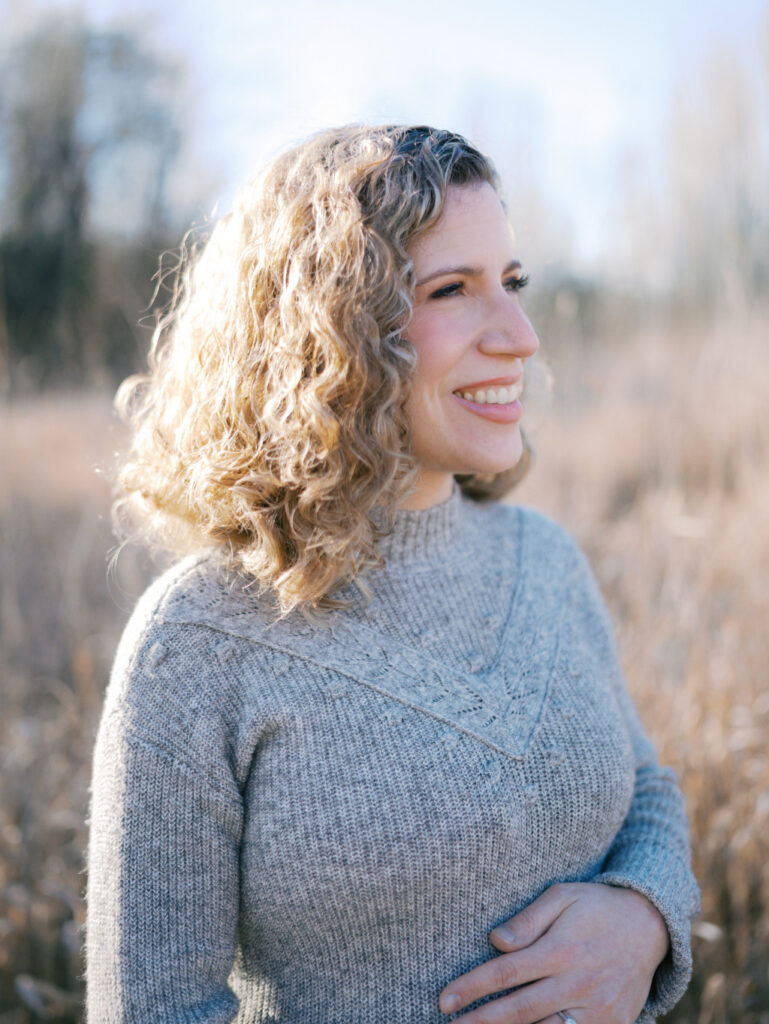 Pregnant woman standing in a grassy field and looking in the distance thinking about Seattle prenatal massage