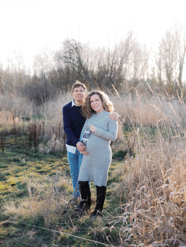 Expecting couple standing in a grassy field getting their maternity photos captured