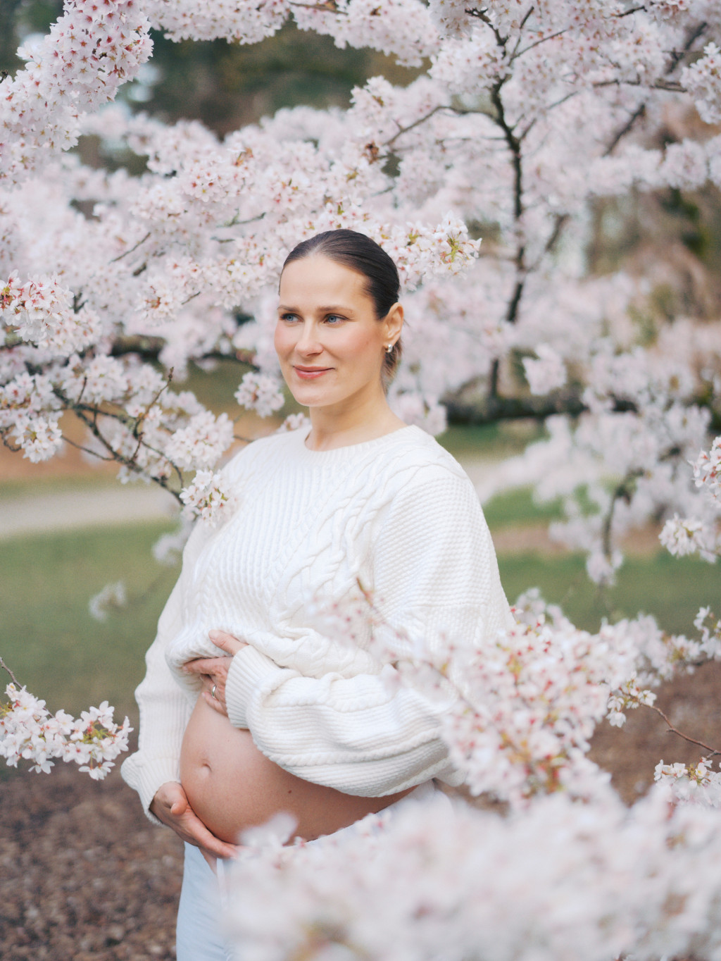 Woman dressed in a cozy knit sweater standing in the middle of a cherry blossom tree