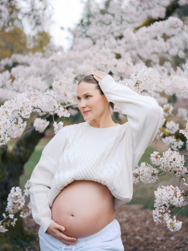 Editorial maternity post of a pregnant woman with her belly out looking in the distance surrounded by cherry blossoms
