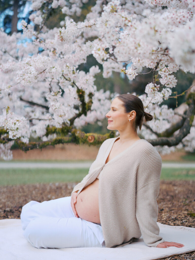 Pregnant woman sitting on a blanket surrounded by cherry blossom trees