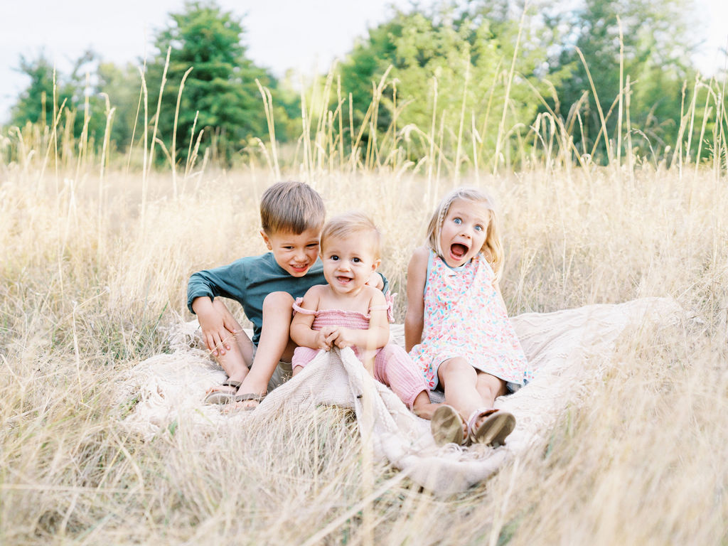 Three kids sitting on the blanket laughing
