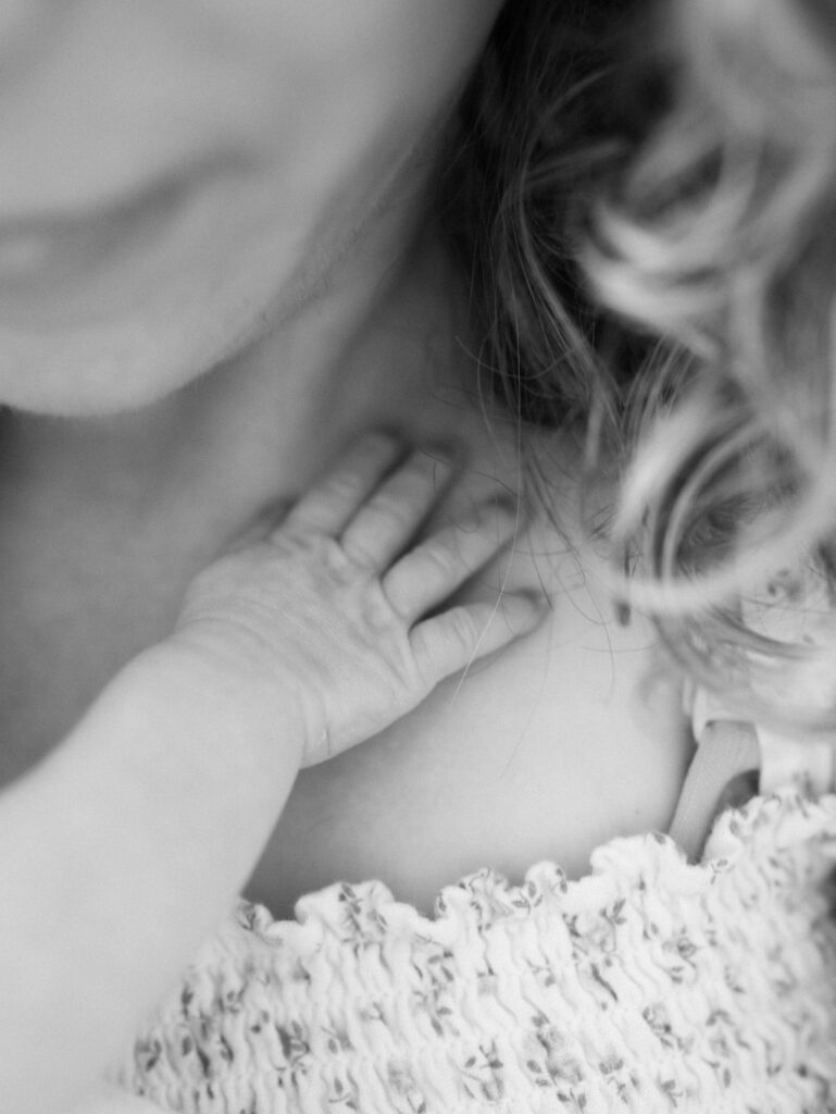 Black and white image of a newborn baby hand on mom's neck