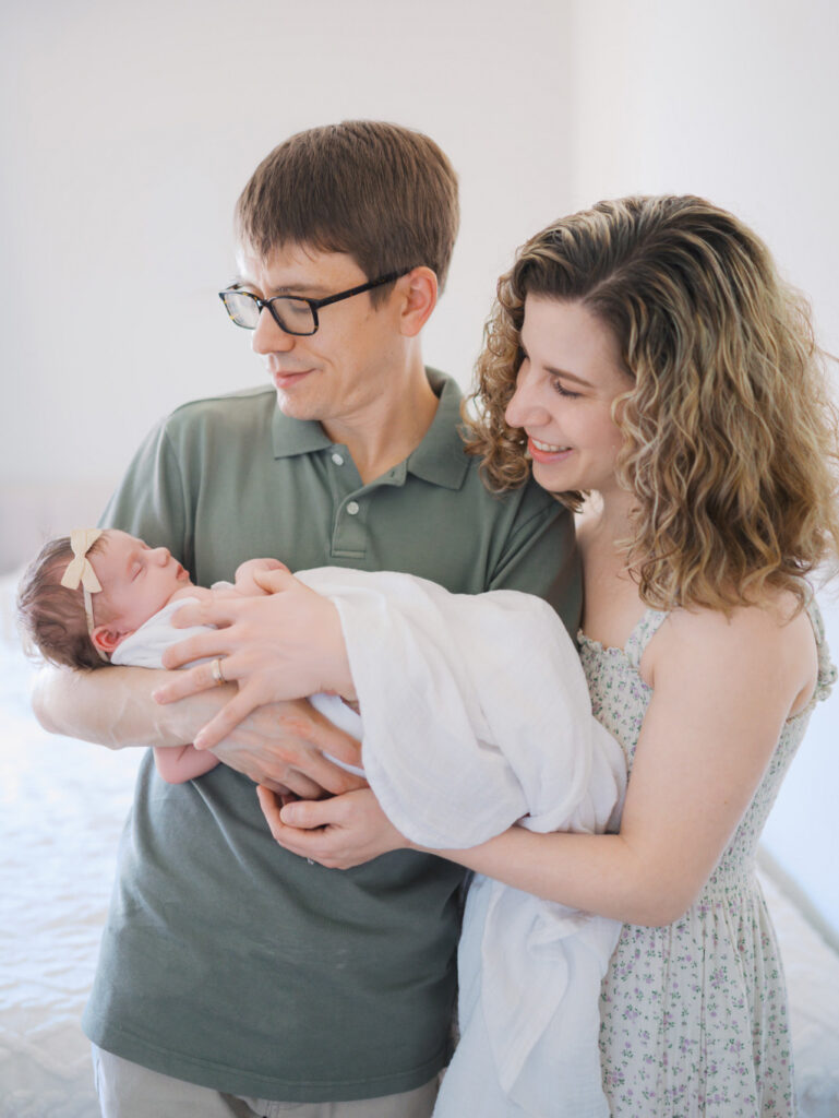 Mom and dad holding an infant baby girl smiling during a seattle newborn session at home