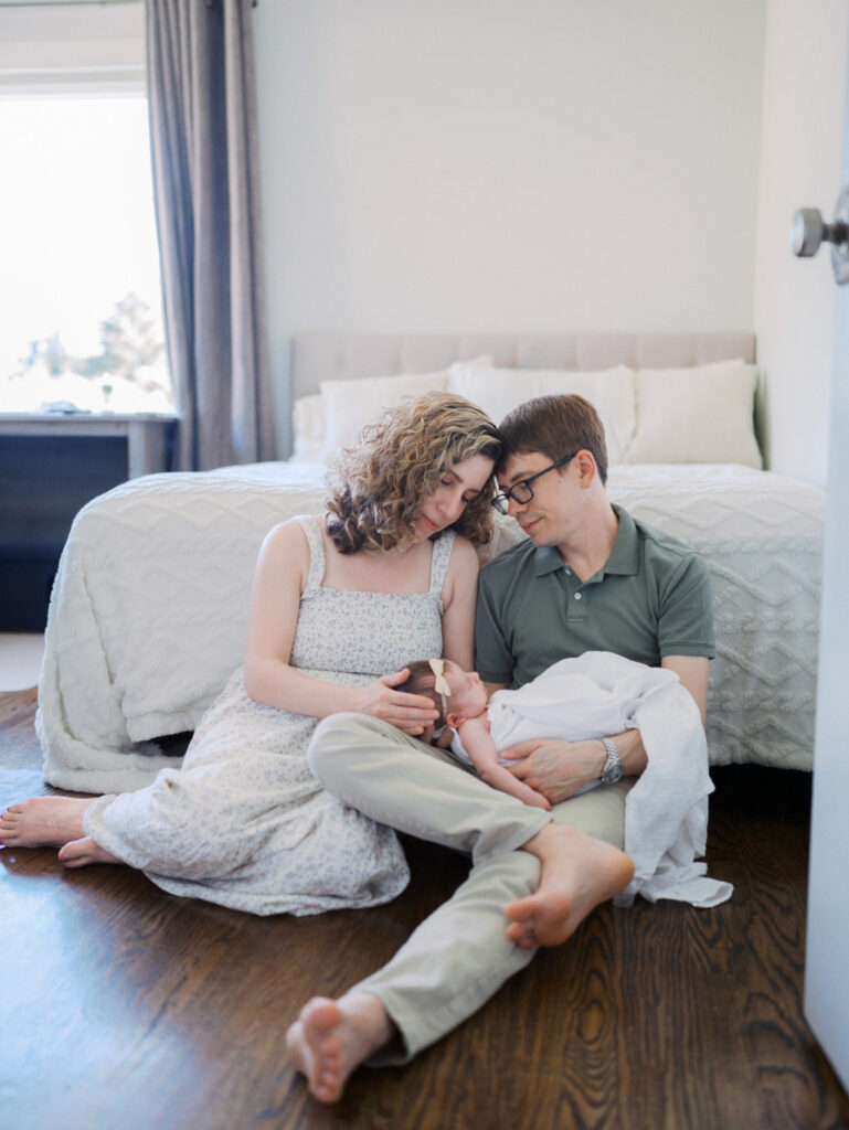 Mom and dad sitting on the floor of the nursery holding their newborn baby girl during their Seattle Baby Photography session