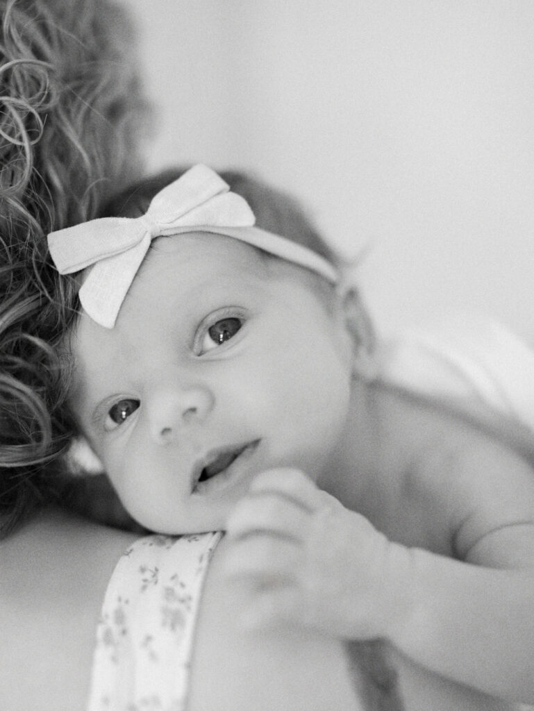 Black and white image of a baby resting on mom's shoulder and making eye contact