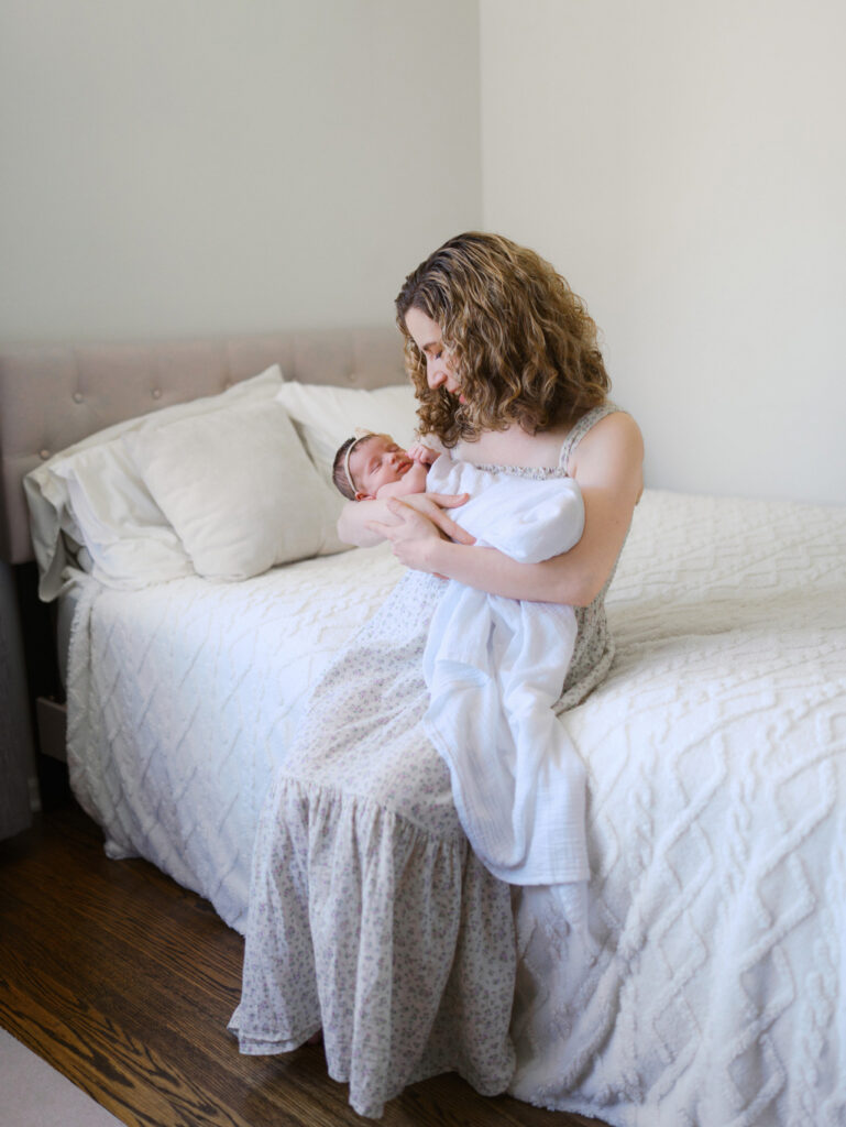 Mom sitting on the bed cradling her newborn baby girl during the Seattle Newborn Session with photographer Tanya Zagumenov