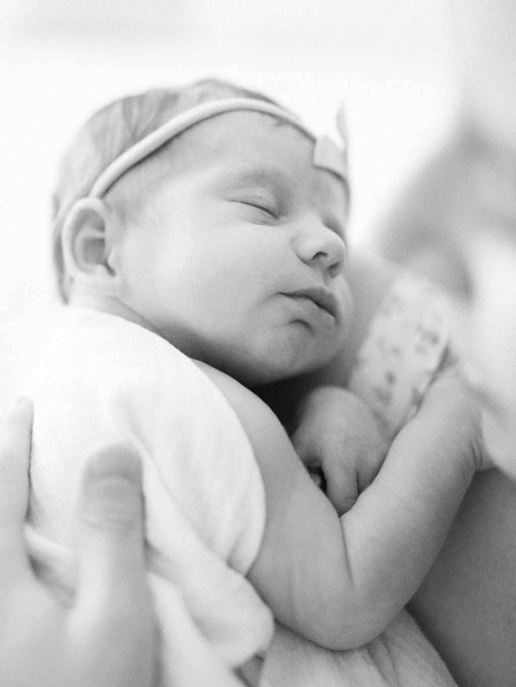 Black and white image of a newborn baby wrapped in a white swaddle blanket snuggling with her mom after being born at a Seattle birth center