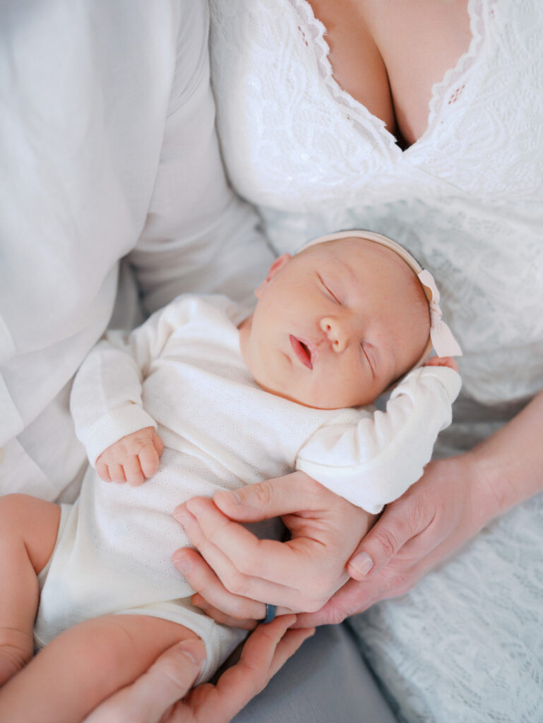Baby sleeping in her parents arms, everyone is dressed in white