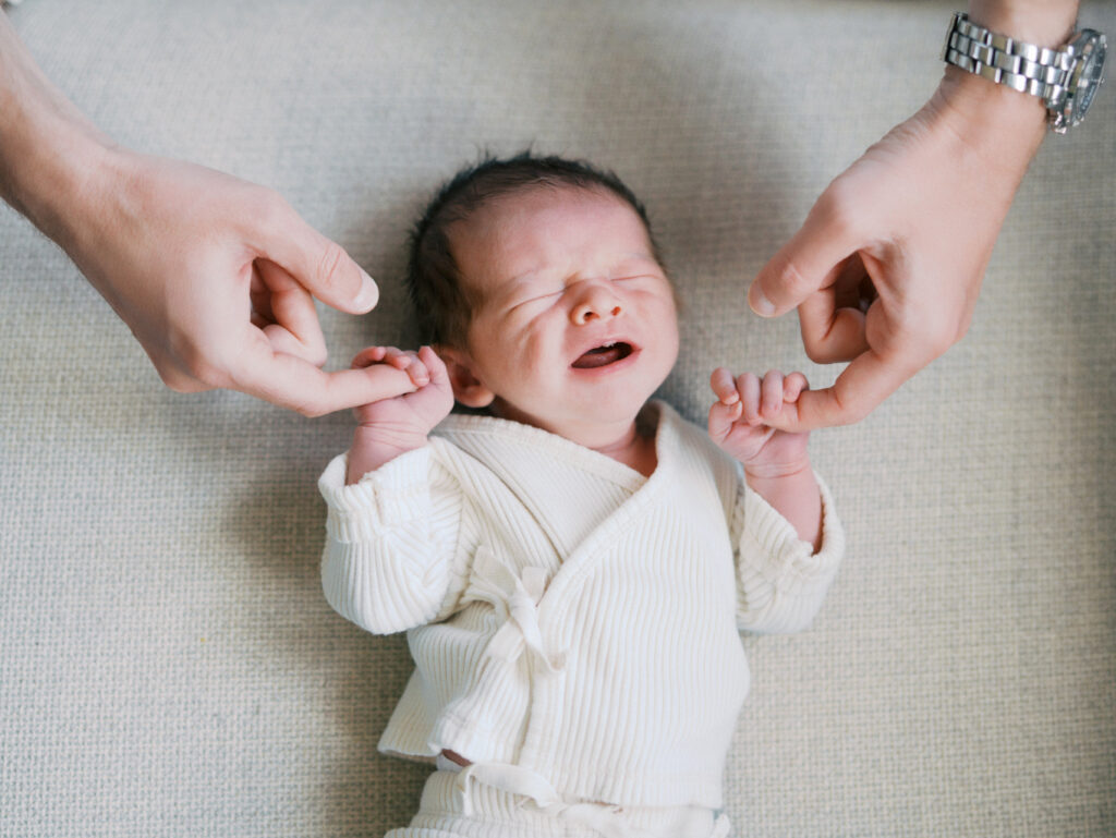 Mom and dad holding newborn baby's hands while baby cries