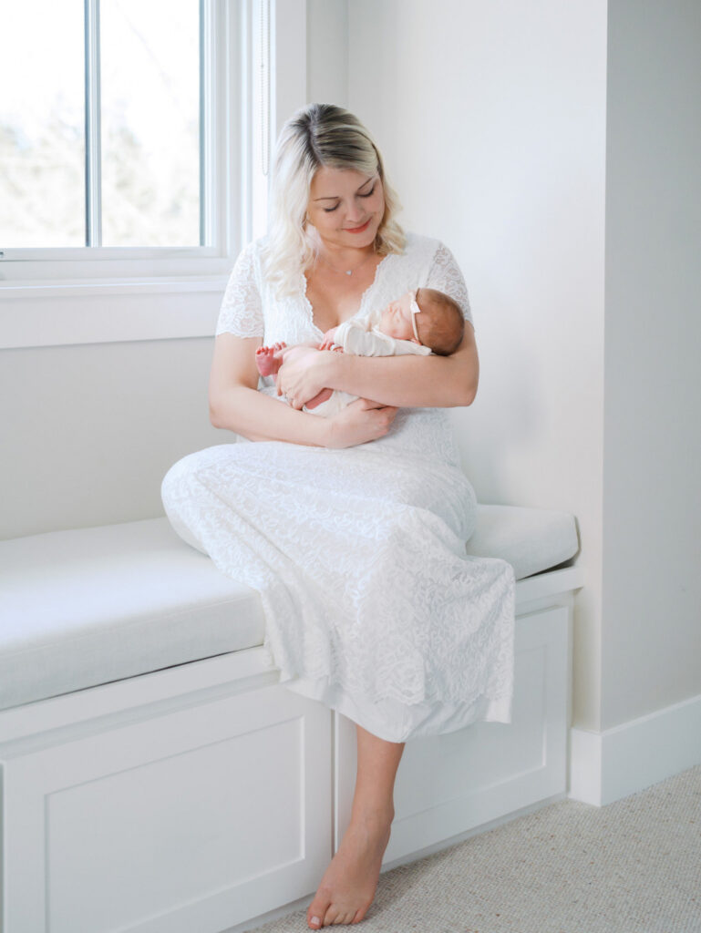 Mom sitting on the ledge of a window cuddling her newborn daughter after giving birth at a Seattle birth center