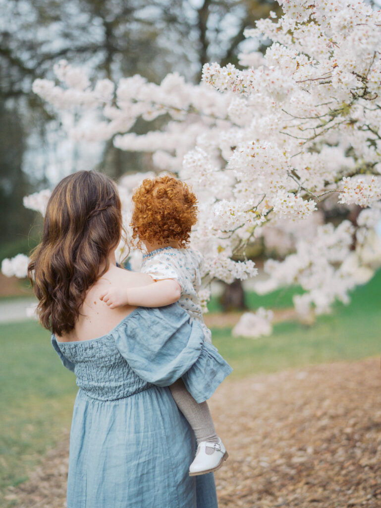 Back of mom and her toddler girl, walking around the park talking about Seattle OBgyns
