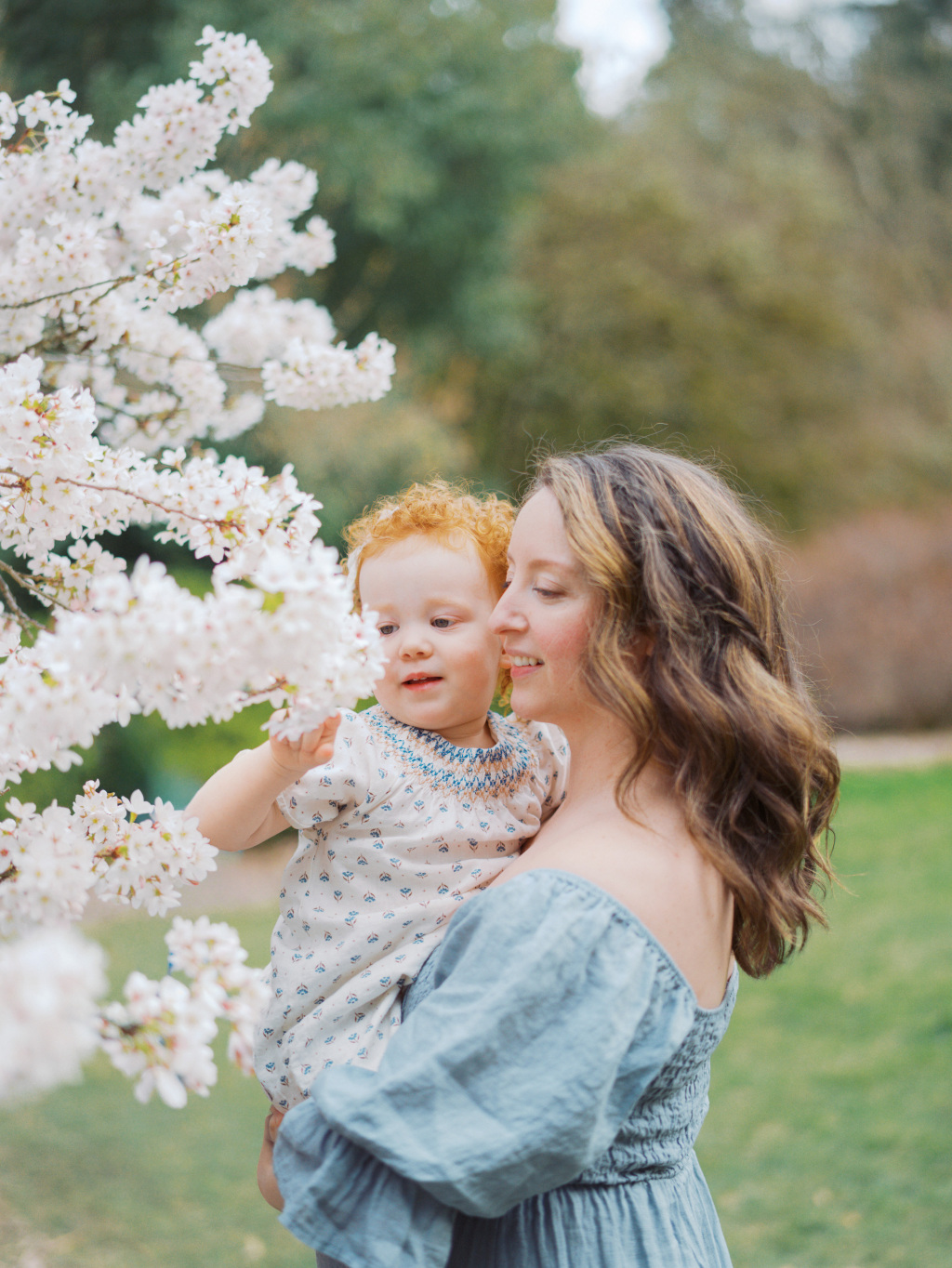 Mom holding a toddler in a parks surrounded by cherry blossoms after researching her options for Seattle Obgyn