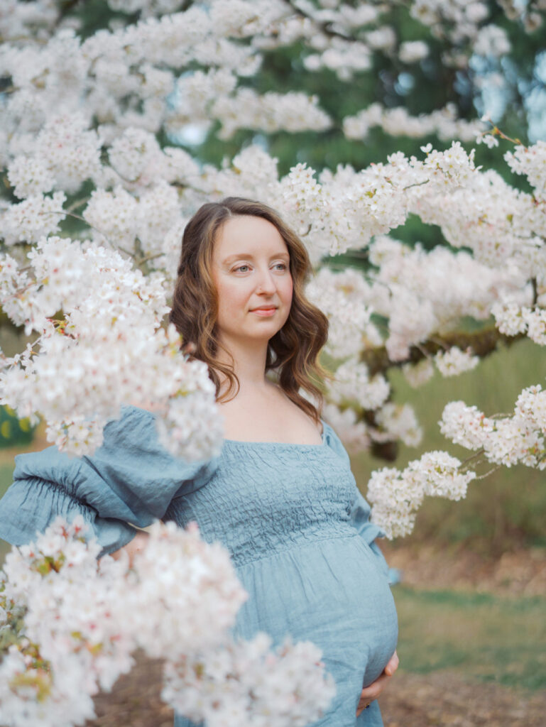 Gorgeous pregnant standing surrounded by cherry blossoms contemplating OBGYNs in Seattle.