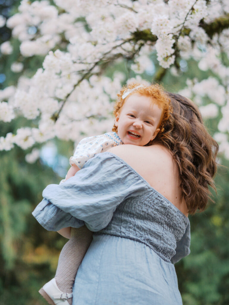 Toddler girl peeking over her pregnant mom's shoulder, laughint