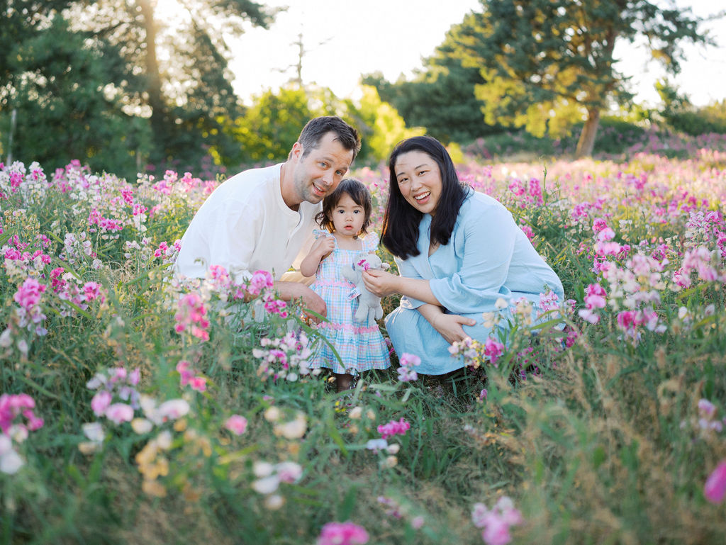 Mom, dad and their toddler daughter exploring sweet pea flowers in Seattle's Discovery park